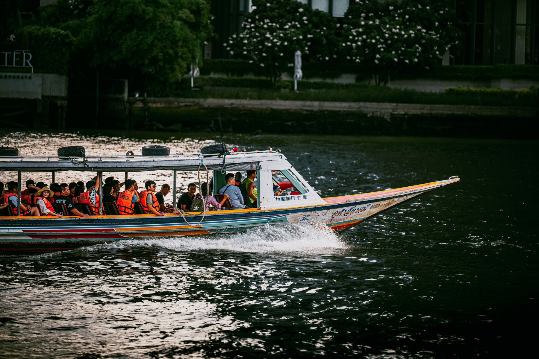 Passengers on a long boat speeding along a river in Bangkok