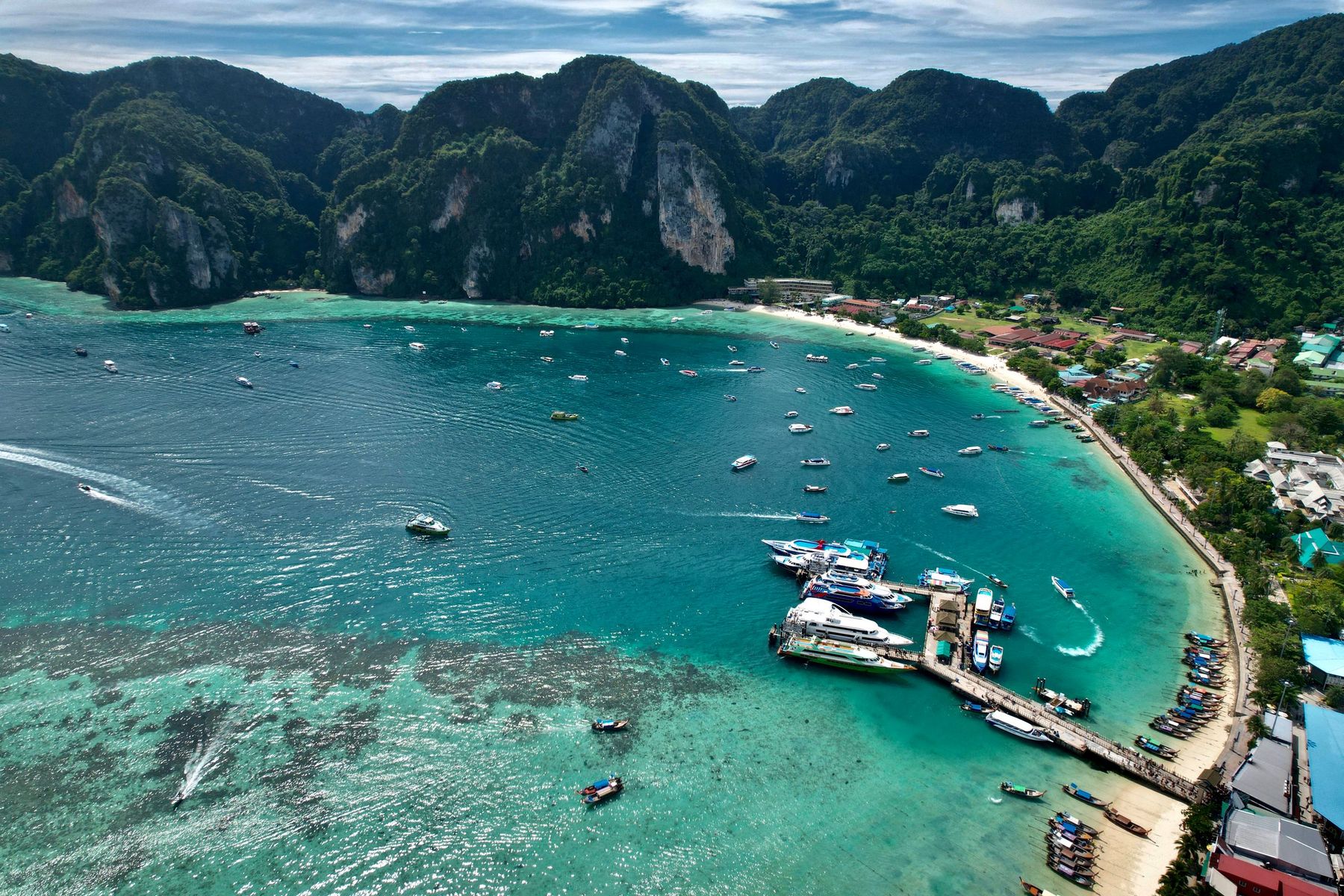 Boats moored in a turquoise bay below green hills, seen from above