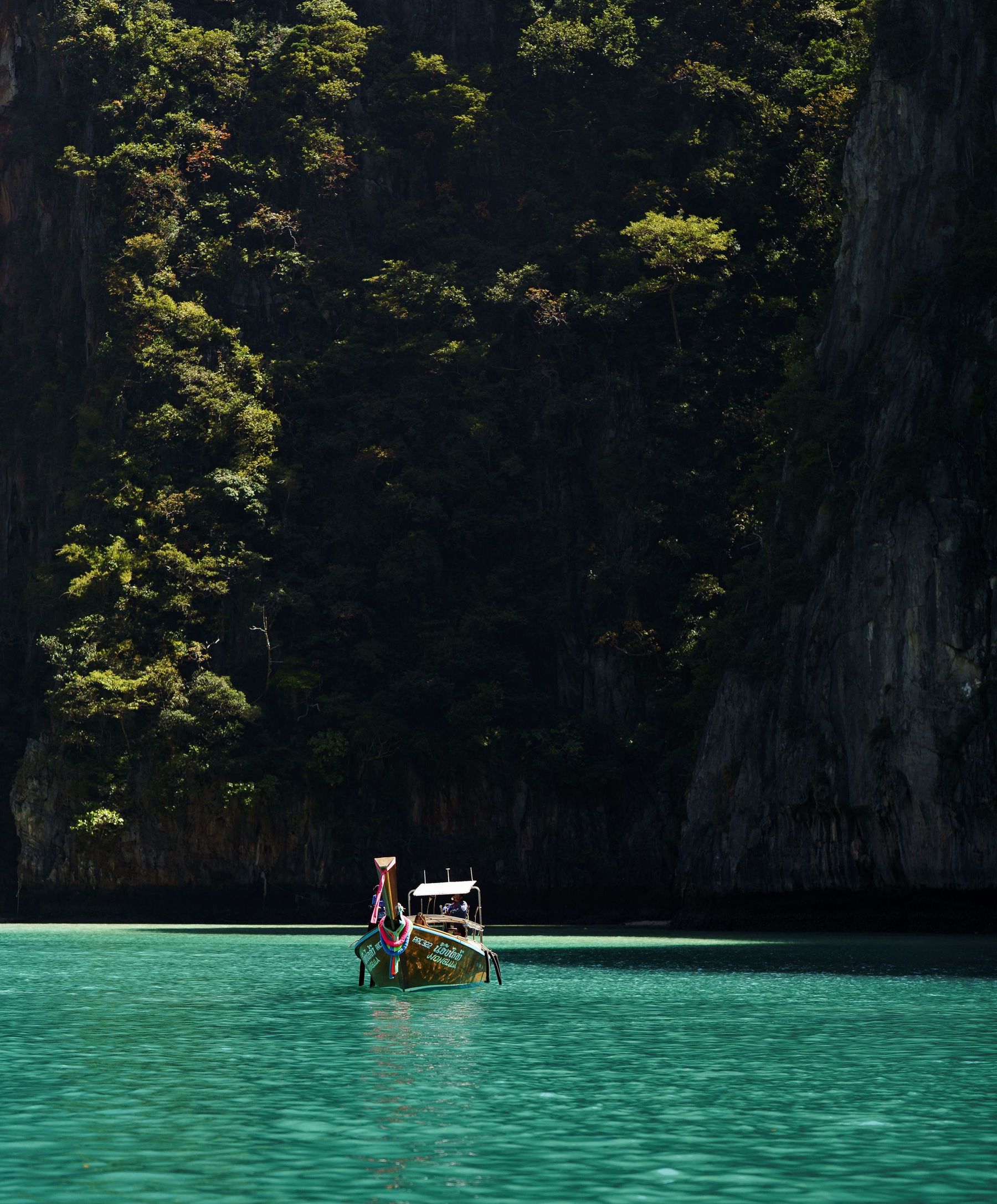 A longtail boat floating in a green lagoon between cliffs