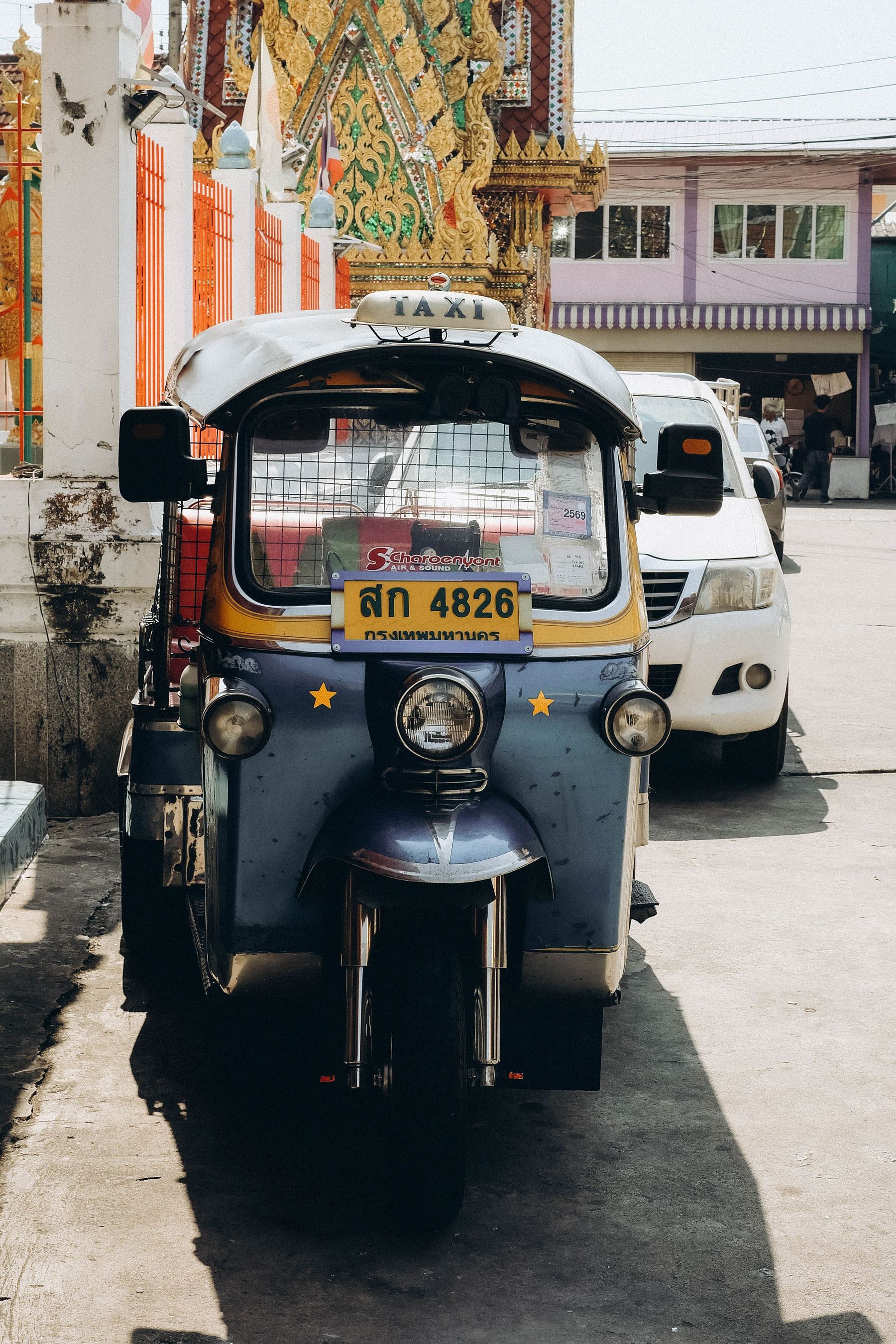 A tuk-tuk parked on a sunny street with a temple behind