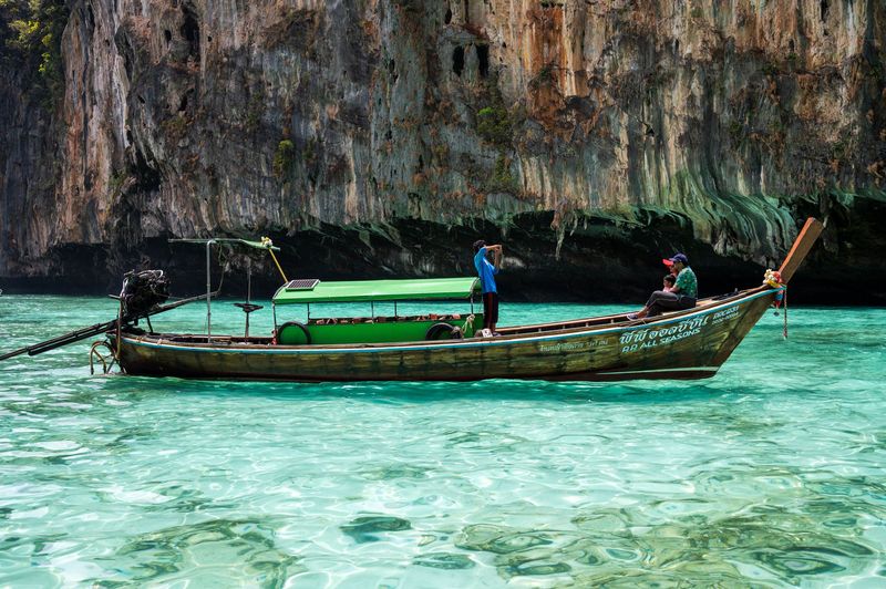 A longtail boat on clear turquoise water below limestone cliffs