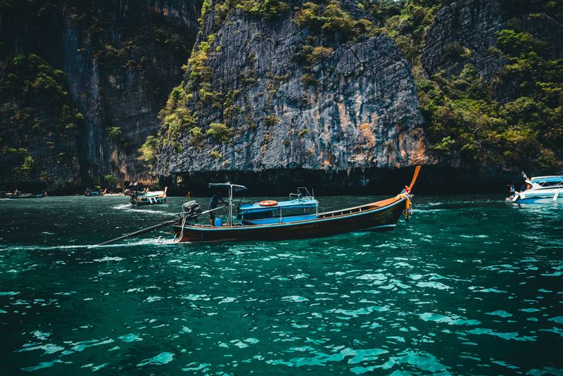 A longtail boat on blue water beside green limestone cliffs