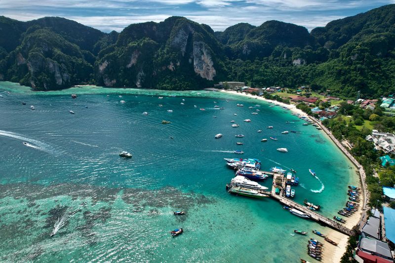Boats moored in a turquoise bay below green hills, seen from above