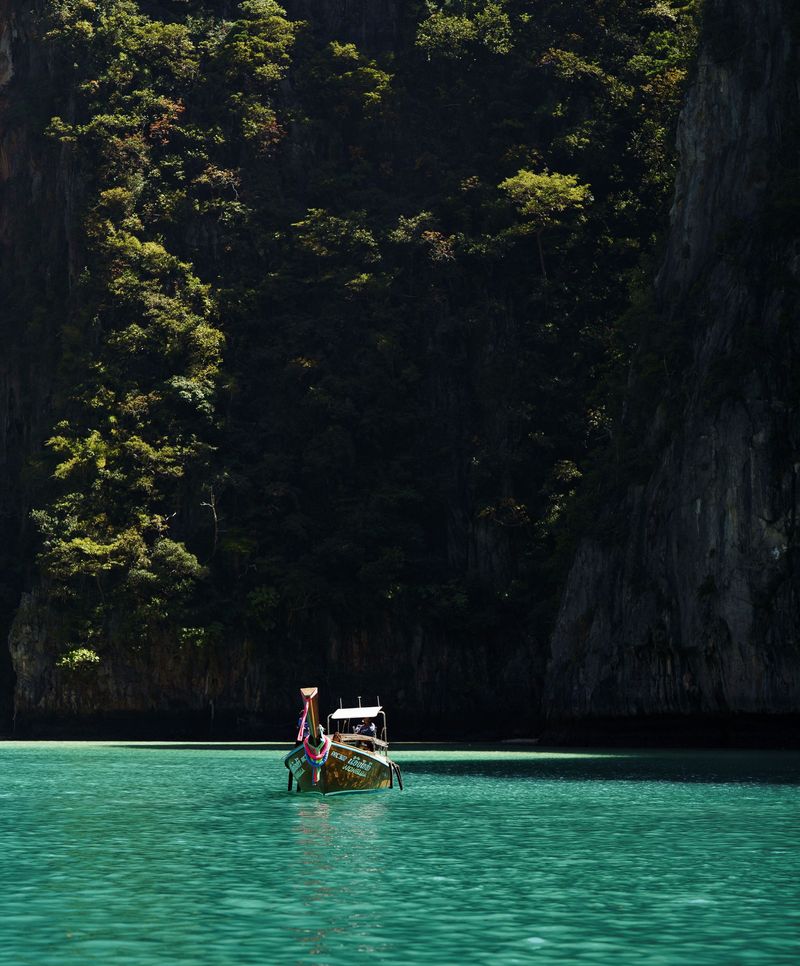 A longtail boat floating in a green lagoon between cliffs