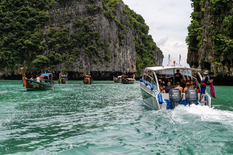 A speedboat full of passengers passing between limestone cliffs