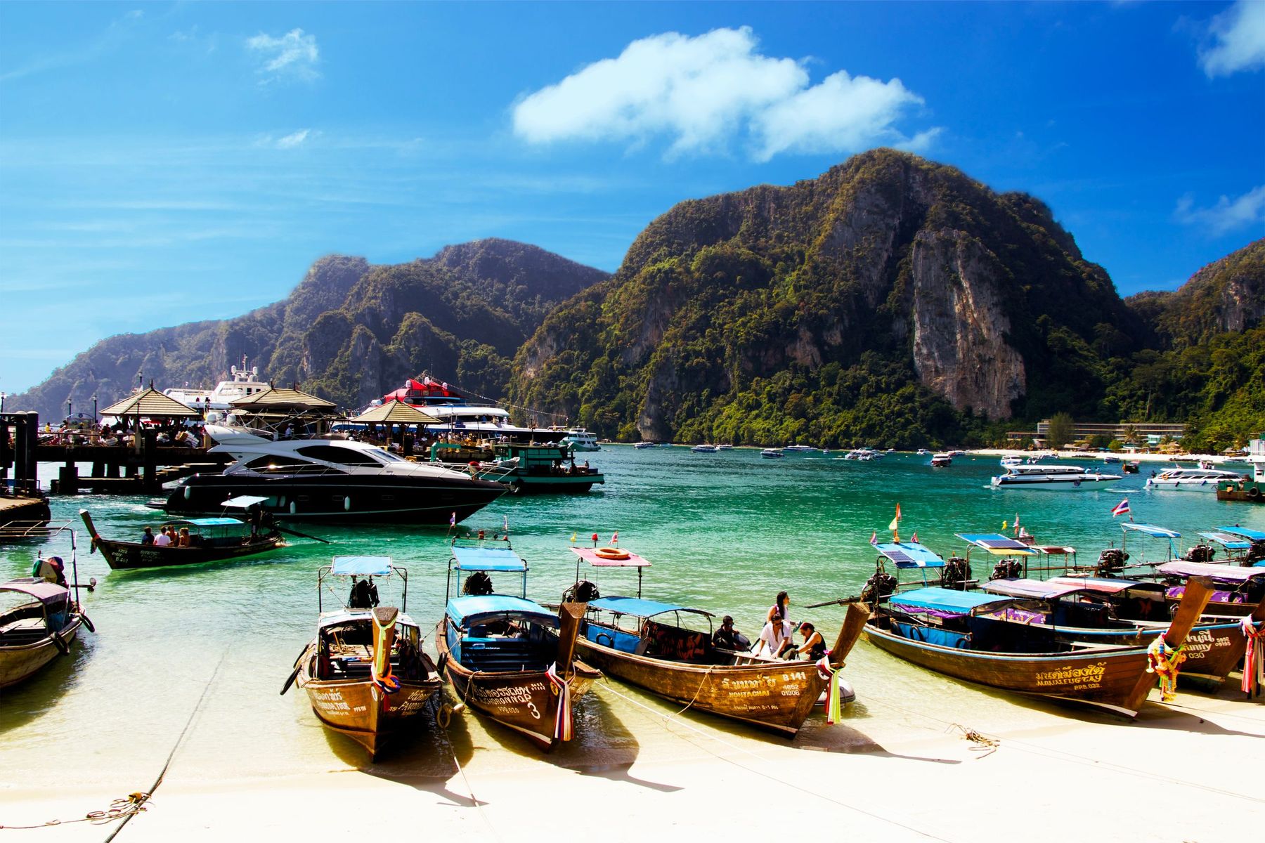 Colourful longtail boats pulled up on a beach below green limestone hills